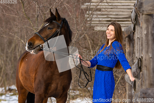Image of A happy girl holds a horse by the bridle and smiles, against the backdrop of a winter forest