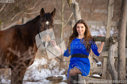 Image of A beautiful girl is sitting on a log against the background of wooden ruins, a horse is standing nearby