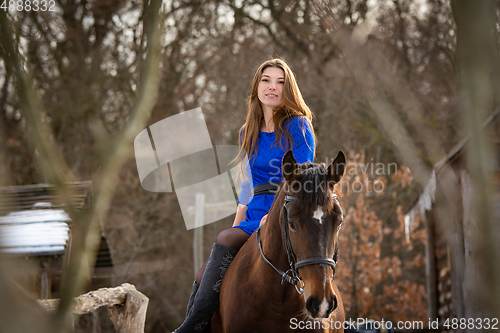 Image of A girl in a blue dress sits on a horse against the backdrop of a winter forest