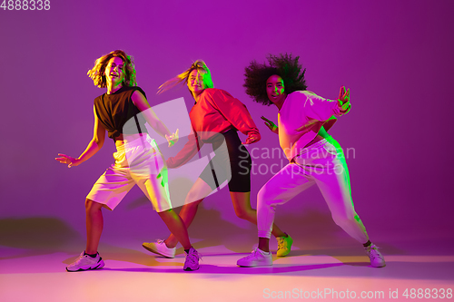 Image of Sportive girls dancing hip-hop in stylish clothes on gradient background at dance hall in neon light