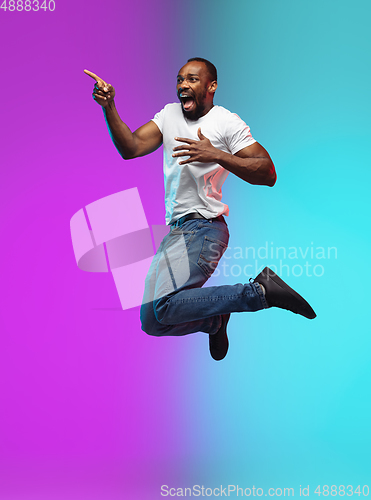 Image of African-american young man\'s portrait on gradient studio background in neon, jumping high