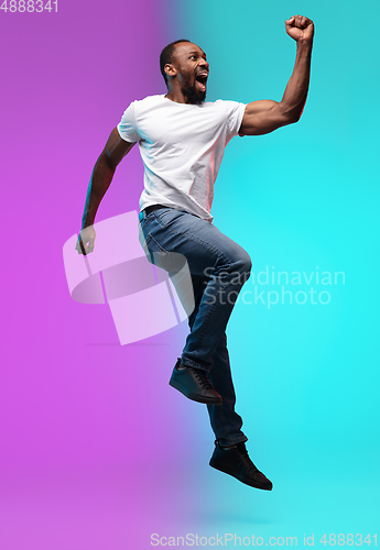 Image of African-american young man\'s portrait on gradient studio background in neon, jumping high
