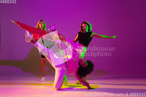 Image of Sportive girls dancing hip-hop in stylish clothes on gradient background at dance hall in neon light