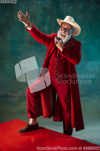 Image of Modern stylish Santa Claus in red fashionable suit and cowboy\'s hat on dark background