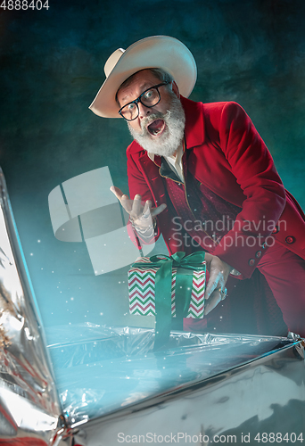 Image of Modern stylish Santa Claus in red fashionable suit and cowboy\'s hat on dark background