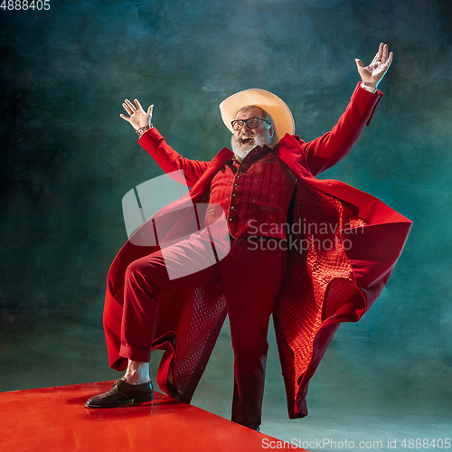 Image of Modern stylish Santa Claus in red fashionable suit and cowboy\'s hat on dark background