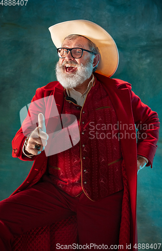 Image of Modern stylish Santa Claus in red fashionable suit and cowboy\'s hat on dark background