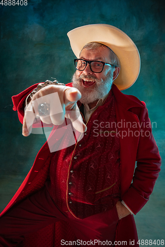 Image of Modern stylish Santa Claus in red fashionable suit and cowboy\'s hat on dark background