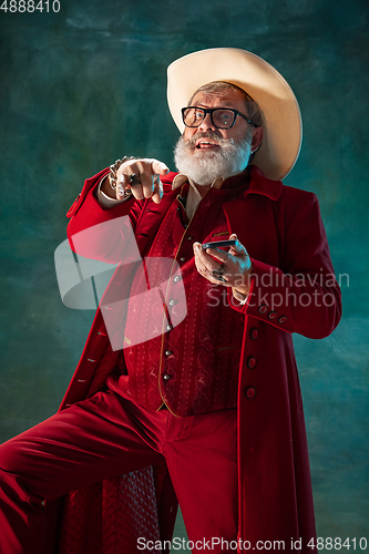 Image of Modern stylish Santa Claus in red fashionable suit and cowboy\'s hat on dark background