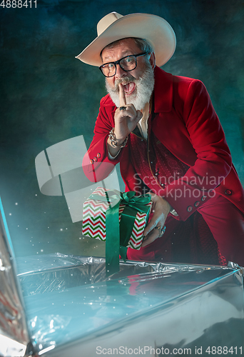 Image of Modern stylish Santa Claus in red fashionable suit and cowboy\'s hat on dark background