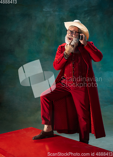 Image of Modern stylish Santa Claus in red fashionable suit and cowboy\'s hat on dark background