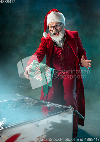 Image of Modern stylish Santa Claus in red fashionable suit and cowboy\'s hat on dark background