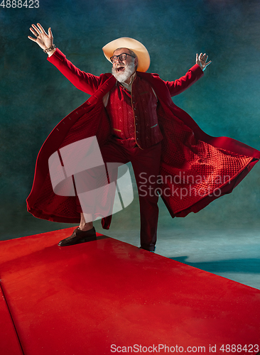 Image of Modern stylish Santa Claus in red fashionable suit and cowboy\'s hat on dark background