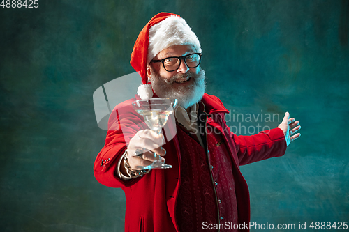 Image of Modern stylish Santa Claus in red fashionable suit and cowboy\'s hat on dark background