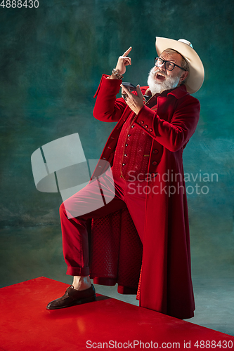 Image of Modern stylish Santa Claus in red fashionable suit and cowboy\'s hat on dark background