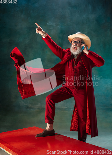 Image of Modern stylish Santa Claus in red fashionable suit and cowboy\'s hat on dark background