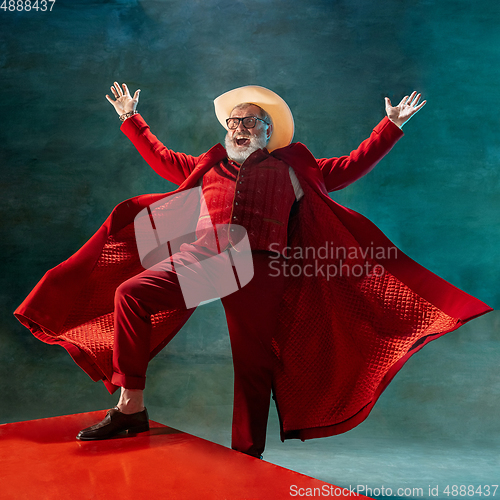 Image of Modern stylish Santa Claus in red fashionable suit and cowboy\'s hat on dark background