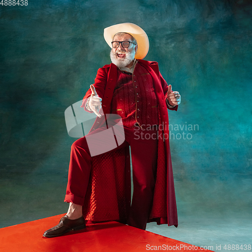 Image of Modern stylish Santa Claus in red fashionable suit and cowboy\'s hat on dark background