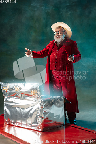 Image of Modern stylish Santa Claus in red fashionable suit and cowboy\'s hat on dark background