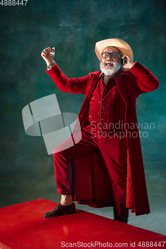 Image of Modern stylish Santa Claus in red fashionable suit and cowboy\'s hat on dark background