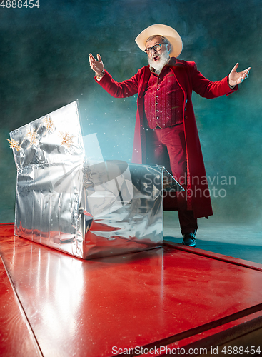 Image of Modern stylish Santa Claus in red fashionable suit and cowboy\'s hat on dark background