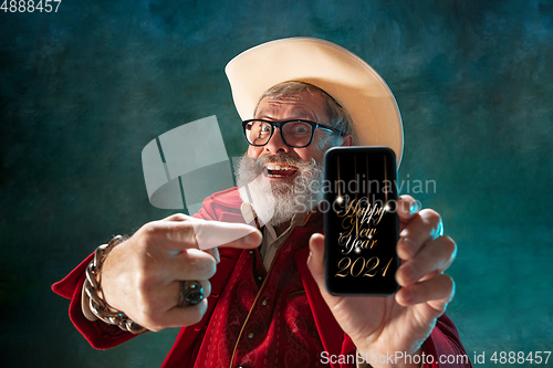 Image of Modern stylish Santa Claus in red fashionable suit and cowboy\'s hat on dark background