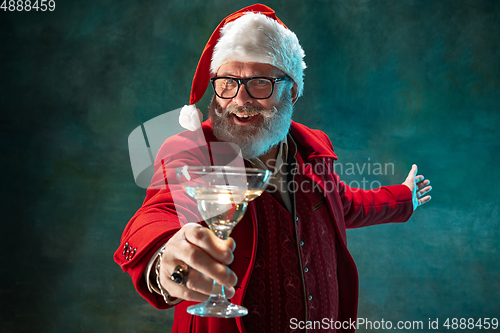 Image of Modern stylish Santa Claus in red fashionable suit and cowboy\'s hat on dark background