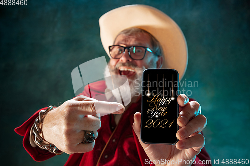 Image of Modern stylish Santa Claus in red fashionable suit and cowboy\'s hat on dark background