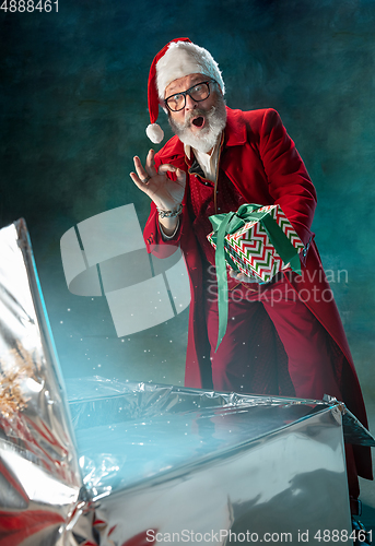 Image of Modern stylish Santa Claus in red fashionable suit and cowboy\'s hat on dark background