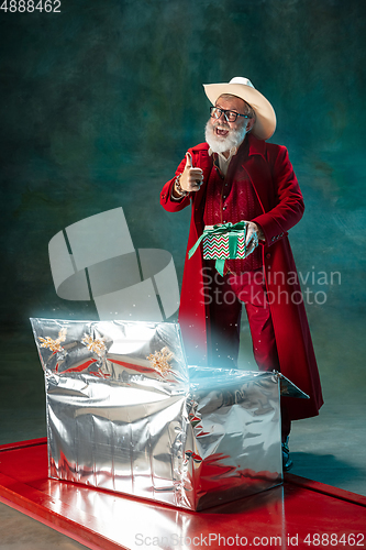 Image of Modern stylish Santa Claus in red fashionable suit and cowboy\'s hat on dark background