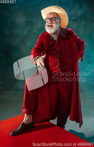 Image of Modern stylish Santa Claus in red fashionable suit and cowboy\'s hat on dark background