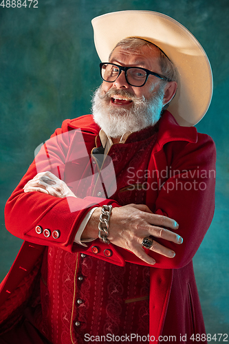 Image of Modern stylish Santa Claus in red fashionable suit and cowboy\'s hat on dark background