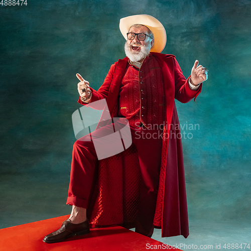 Image of Modern stylish Santa Claus in red fashionable suit and cowboy\'s hat on dark background