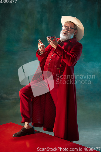 Image of Modern stylish Santa Claus in red fashionable suit and cowboy\'s hat on dark background