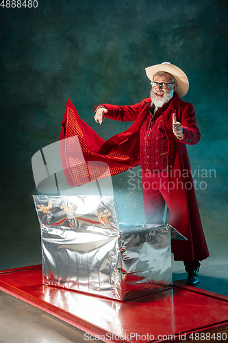 Image of Modern stylish Santa Claus in red fashionable suit and cowboy\'s hat on dark background