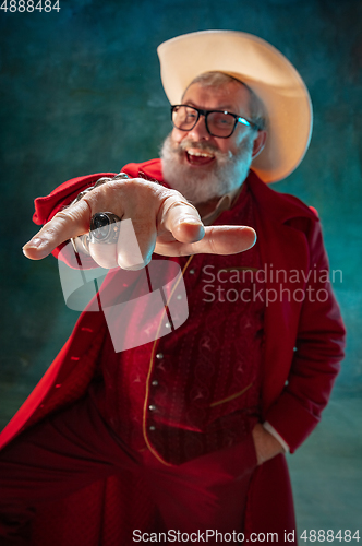 Image of Modern stylish Santa Claus in red fashionable suit and cowboy\'s hat on dark background