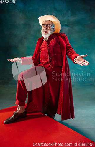 Image of Modern stylish Santa Claus in red fashionable suit and cowboy\'s hat on dark background