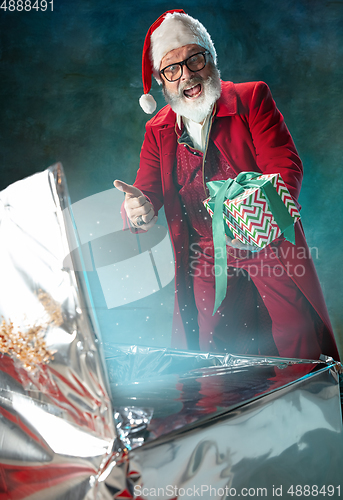 Image of Modern stylish Santa Claus in red fashionable suit and cowboy\'s hat on dark background