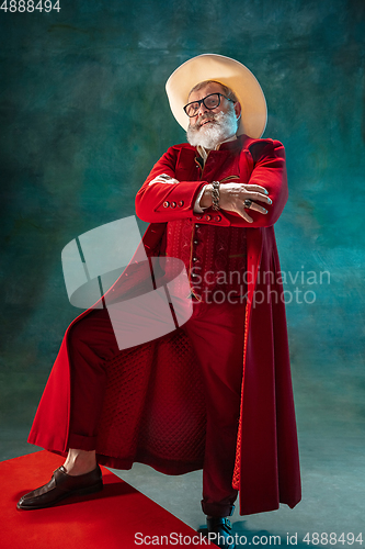 Image of Modern stylish Santa Claus in red fashionable suit and cowboy\'s hat on dark background