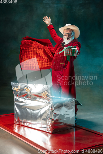 Image of Modern stylish Santa Claus in red fashionable suit and cowboy\'s hat on dark background