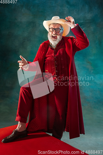 Image of Modern stylish Santa Claus in red fashionable suit and cowboy\'s hat on dark background