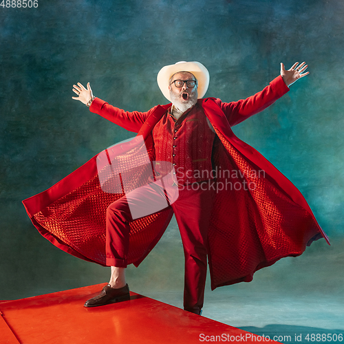 Image of Modern stylish Santa Claus in red fashionable suit and cowboy\'s hat on dark background