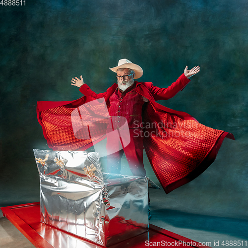 Image of Modern stylish Santa Claus in red fashionable suit and cowboy\'s hat on dark background