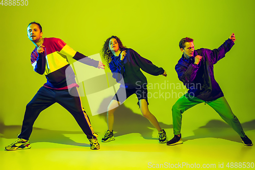 Image of Stylish men and woman dancing hip-hop in bright clothes on gradient background at dance hall in neon light