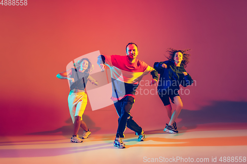 Image of Stylish man and women dancing hip-hop in bright clothes on gradient background at dance hall in neon light