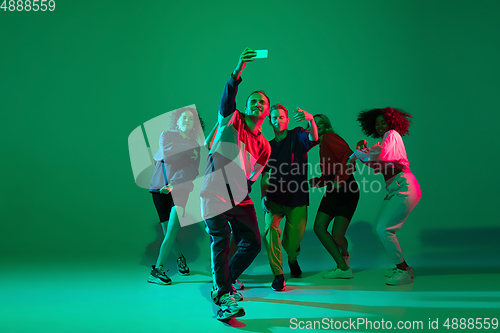 Image of Stylish men and woman dancing hip-hop in bright clothes on gradient background at dance hall in neon light