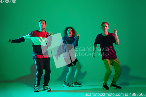 Image of Stylish men and woman dancing hip-hop in bright clothes on gradient background at dance hall in neon light