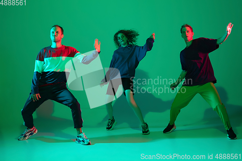 Image of Stylish men and woman dancing hip-hop in bright clothes on gradient background at dance hall in neon light