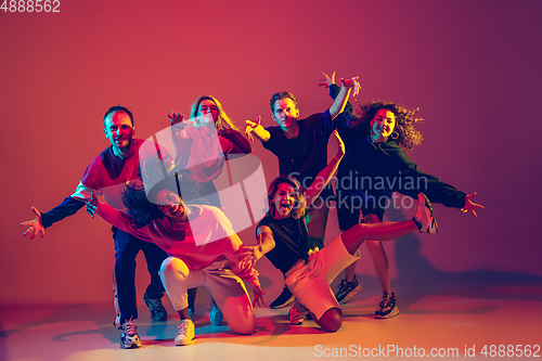 Image of Stylish men and women dancing hip-hop in bright clothes on gradient background at dance hall in neon light