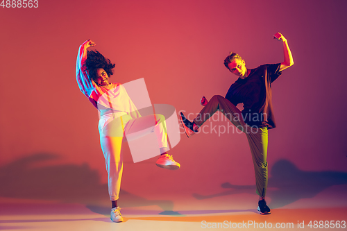 Image of Stylish man and woman dancing hip-hop in bright clothes on gradient background at dance hall in neon light